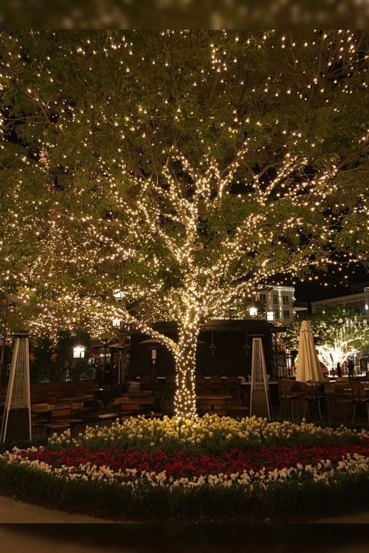 a lighted tree in the middle of a flower garden