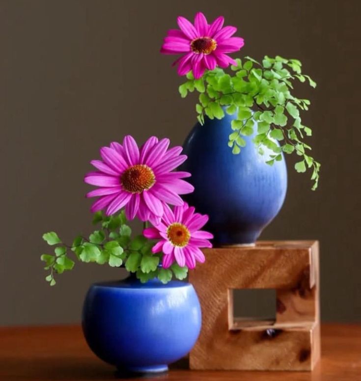 two blue vases with pink flowers in them on a wooden table next to a wood block