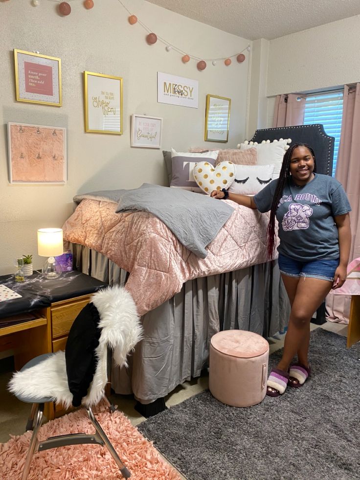 a woman standing next to a bed in a room with pink and gray decor on the walls