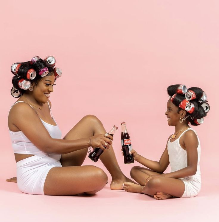 two women are sitting on the floor with hair rollers in their hair and one is holding a beer