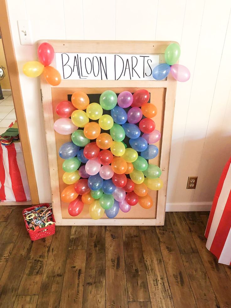 balloons are arranged in a wooden box on the floor next to a sign that says balloon darts