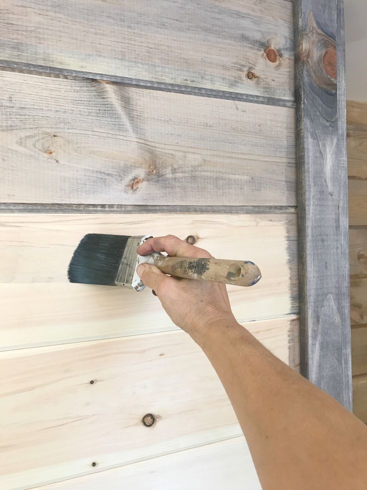 a person holding a paintbrush in their right hand and painting the wood on the wall