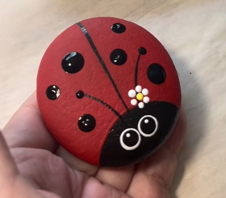 a hand holding a painted rock with a ladybug on it's side