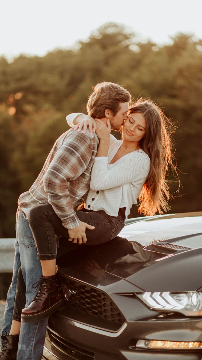 a man and woman kissing on the hood of a car