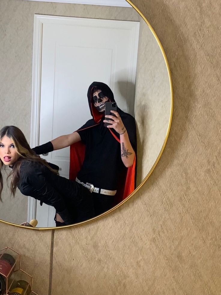 a woman taking a selfie in front of a mirror with a man wearing a mask