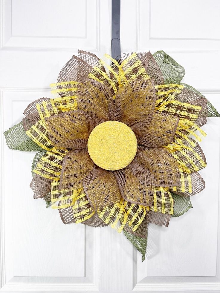 a yellow and green mesh sunflower hanging on a white door with black ribbon around it