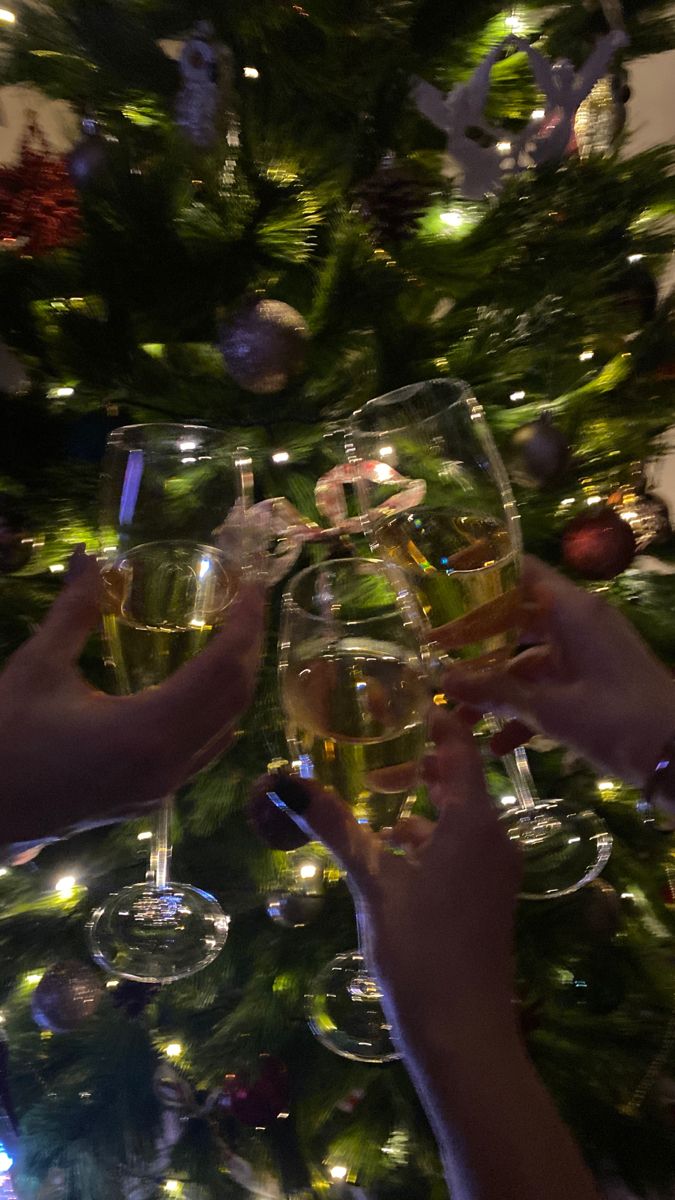 several people toasting with wine glasses in front of a christmas tree