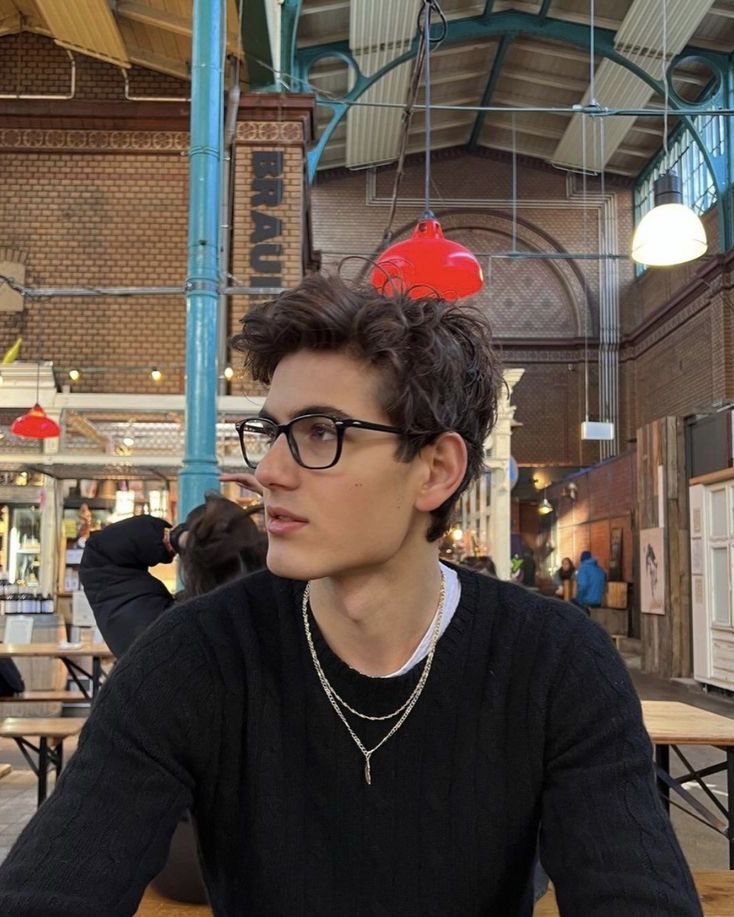 a young man sitting at a table with food on top of his head and looking off to the side