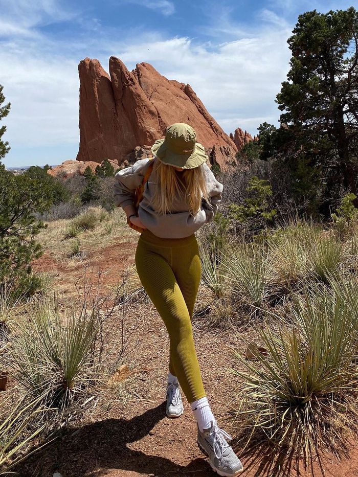 a woman in yellow pants and hat walking through the desert