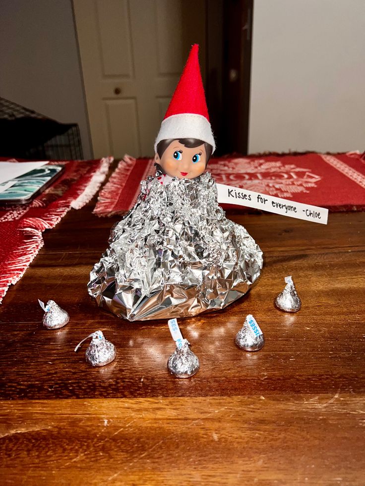 an elf is sitting on top of tin foil with hershey kisses in front of him