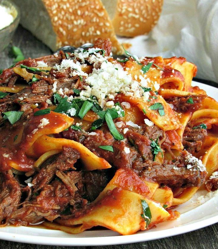 a white plate topped with pasta covered in meat and cheese next to bread on a table