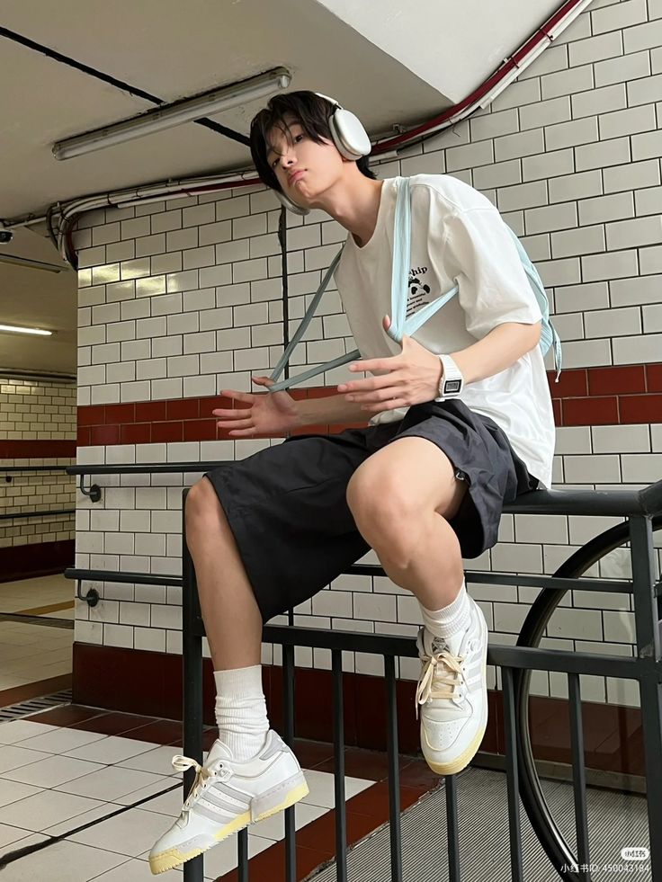 a young man sitting on top of a metal rail next to a white tiled wall