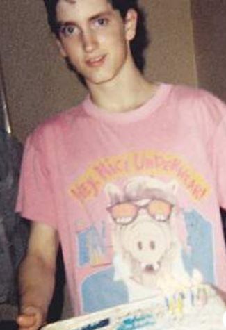 a young man is holding a cake in his hands and smiling at the camera while wearing a pink tshirt