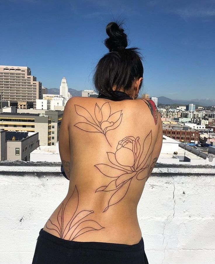 a woman with tattoos on her back standing in front of a cityscape and looking at the sky