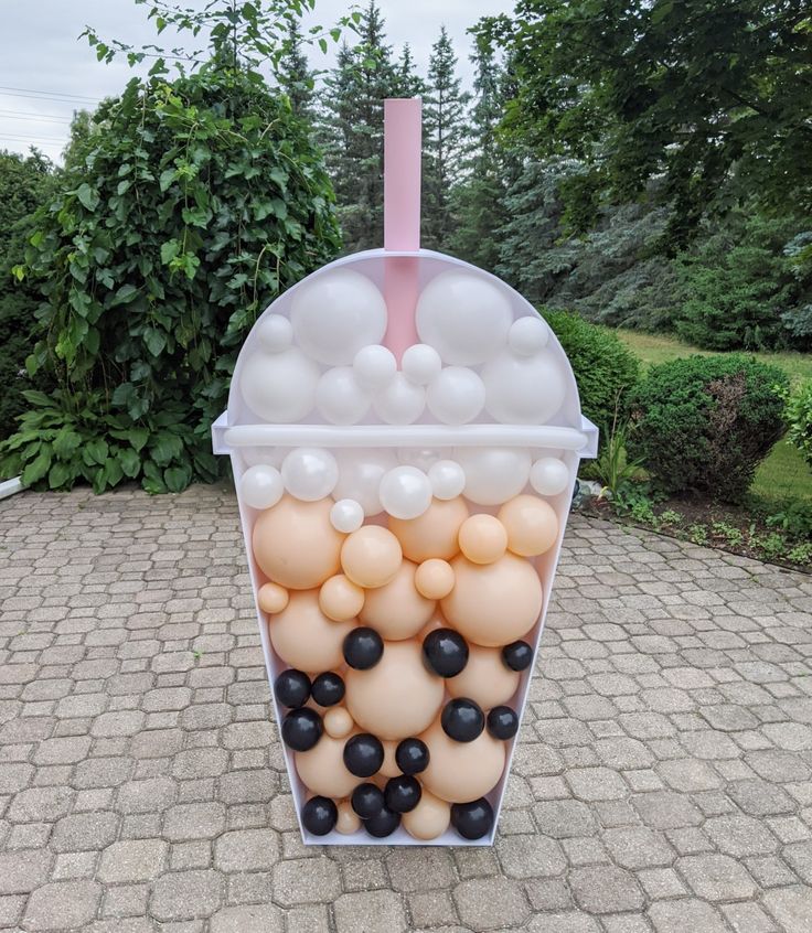 a plastic container filled with balloons on top of a brick walkway next to trees and bushes