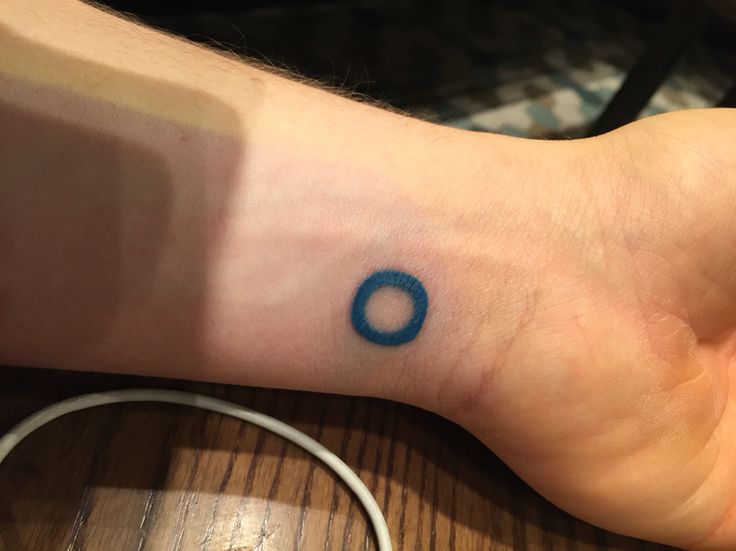 a person's foot with a small blue circle tattoo on the left side of their arm