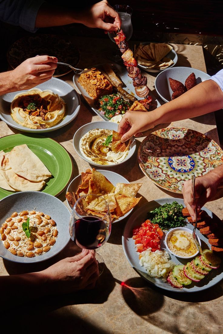 several people are sitting around a table full of food and drinks, with their hands on the plates