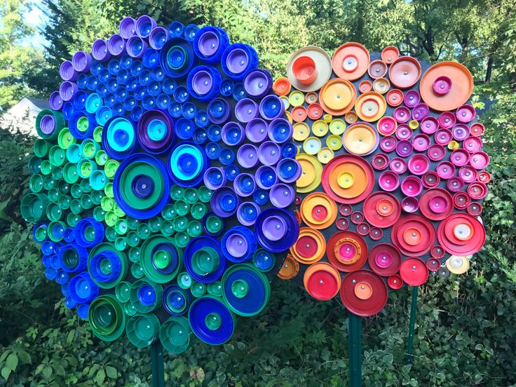 three different colored vases sitting next to each other on top of metal poles in front of trees