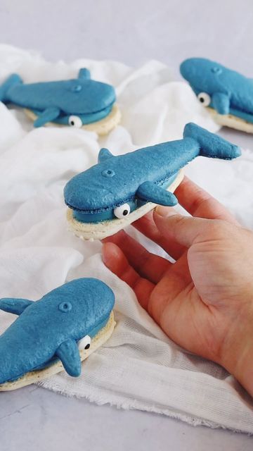 a hand is holding some cookies with blue icing and fake sharks on them,