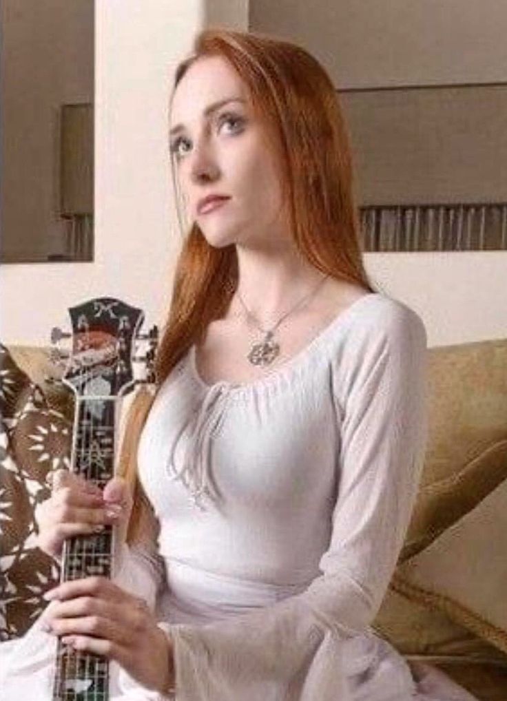 a woman is sitting on a couch with a guitar in her hand and looking at the camera