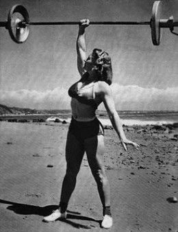 a woman lifting a barbell over her head on the beach