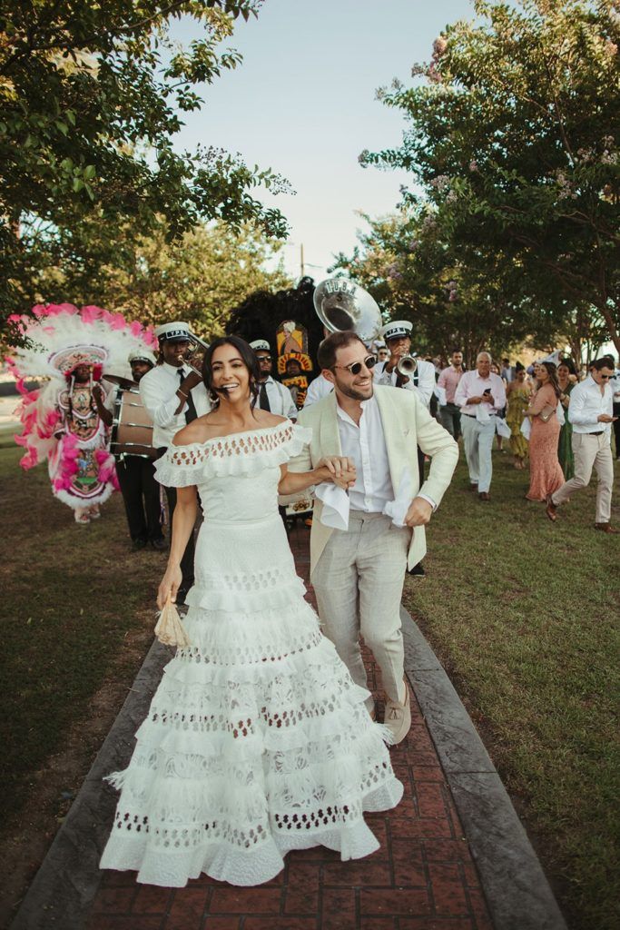 a man and woman walking down a path in white dresses with feathers on their head