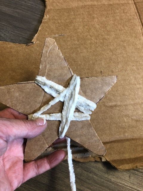 a hand is holding some string wrapped in brown paper with a star shaped object on it