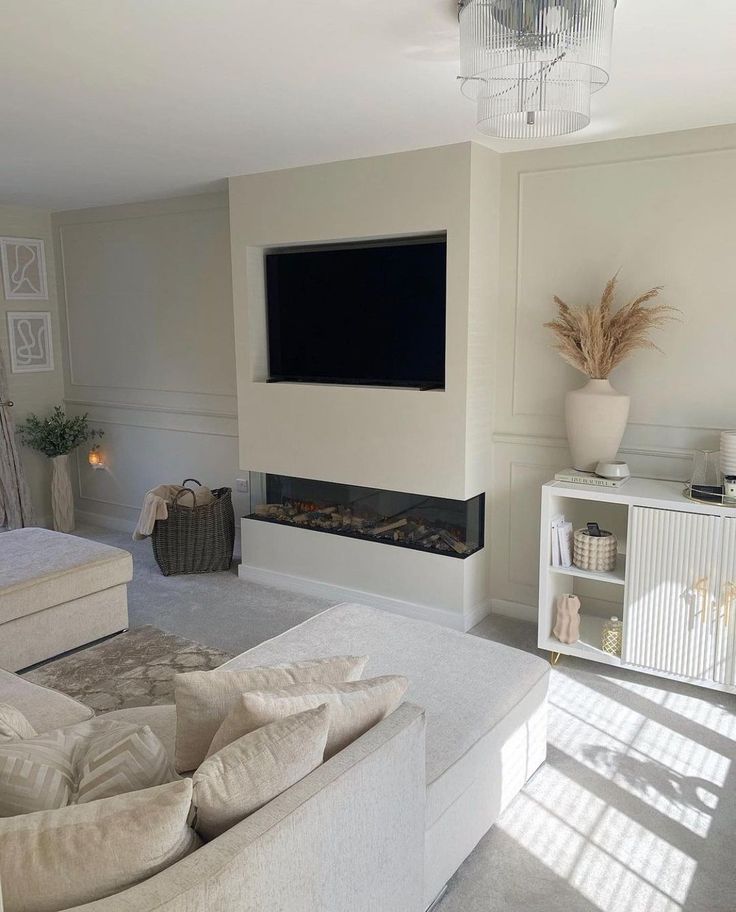 a living room with white furniture and a flat screen tv mounted on the wall above it