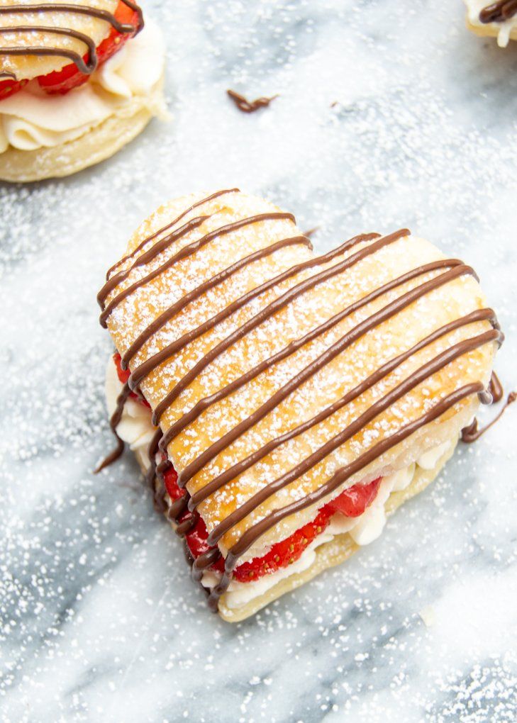 puff pastry hearts with chocolate drizzled on top and strawberries in the background