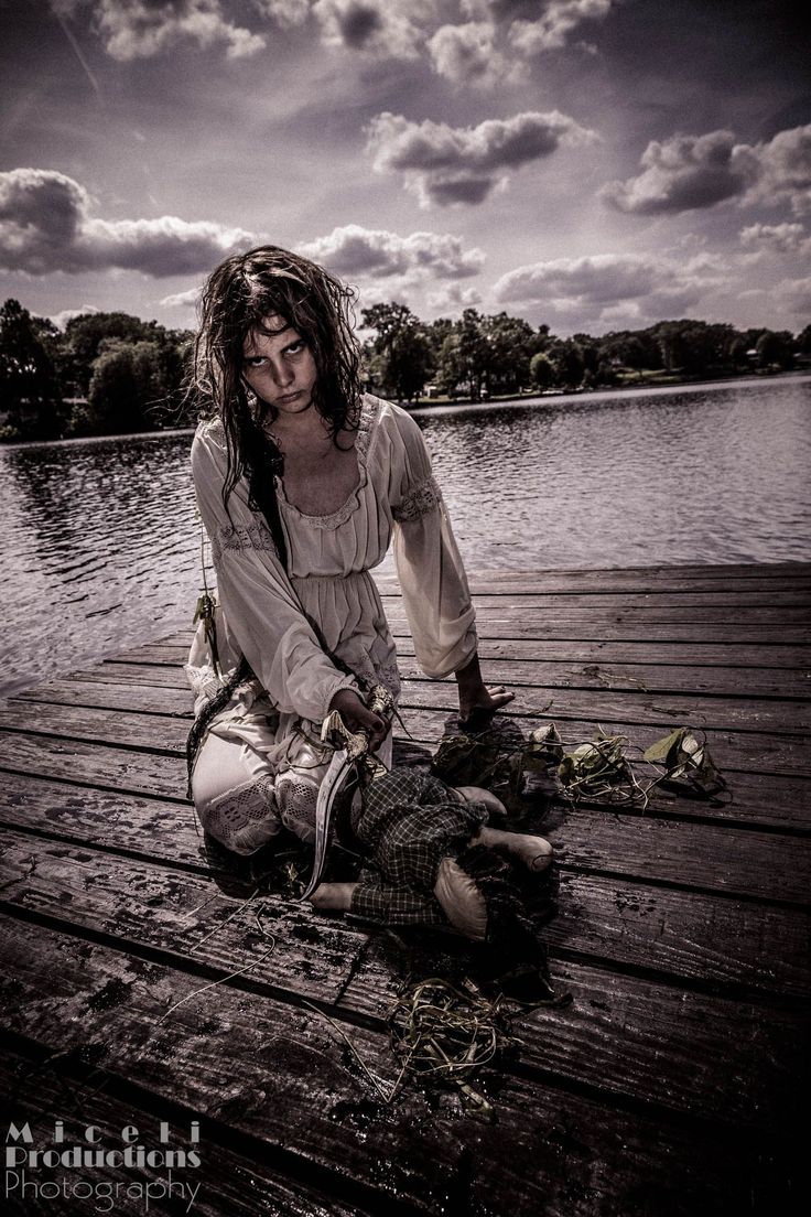 a woman with long hair sitting on a dock next to a body of water holding a fish