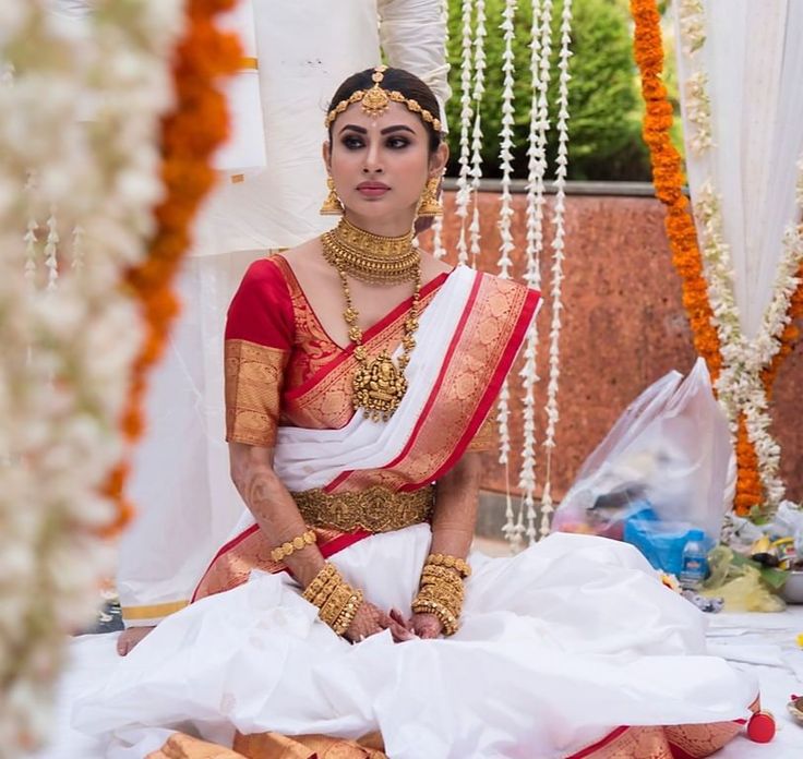 a woman sitting on the ground wearing a white and red sari with gold jewelry