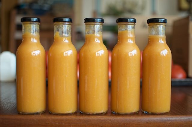 four bottles filled with orange juice sitting on top of a wooden table