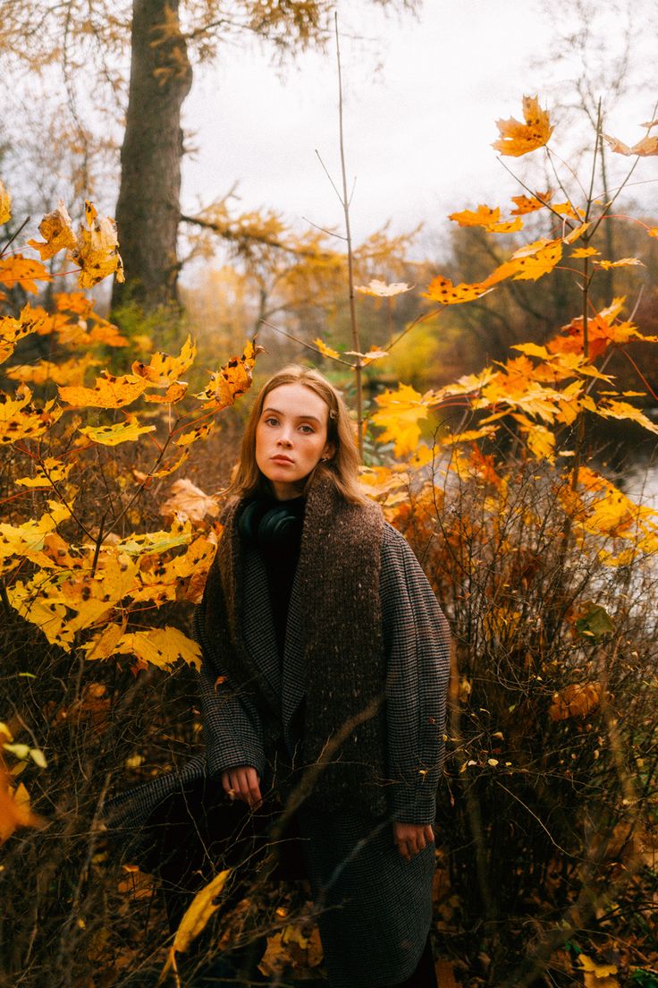 a woman standing in the woods surrounded by yellow leaves