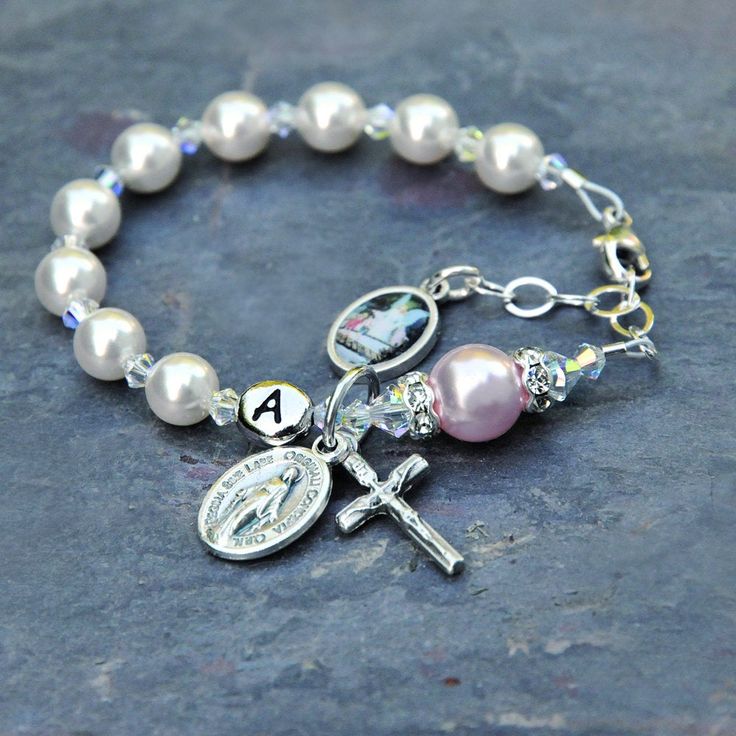 Celebrate the Baptism of a baby girl with this beautiful white and rosaline pink guardian angel rosary bracelet. The bracelet features genuine Swarovski crystals and crystal pearls throughout. The bracelet has white Swarovski pearls for the Hail Mary prayers and just a touch of rosaline pink with the larger Our Father pearl. In between are sparkly Swarovski crystals with an aurora borealis finish. The Our Father pearl is surrounded by crystal rhinestone rondelles. If you select the personalizati Personalized Silver Rosary Bracelet For Confirmation, Personalized Adjustable Rosary Bracelet For Confirmation, Personalized White Pearl Bracelet For Baptism, White Jewelry For Confirmation On Mother's Day, Personalized Spiritual Bracelets For First Communion, Personalized Pink Spiritual Charm Bracelet, Pink Spiritual Jewelry For First Communion, Personalized White Rosary Bracelet For Baptism, White Miraculous Medal Jewelry For First Communion