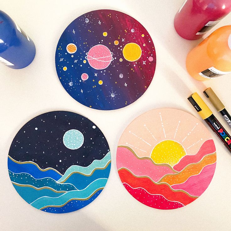 three coasters with different designs on them next to markers and paintbrushes,