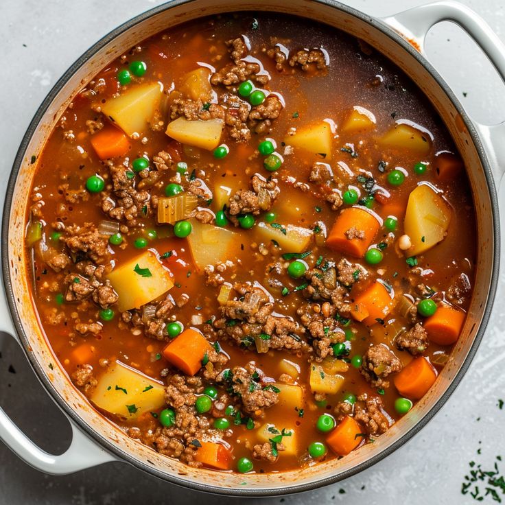 a pot filled with meat and vegetables on top of a white counter next to a spoon