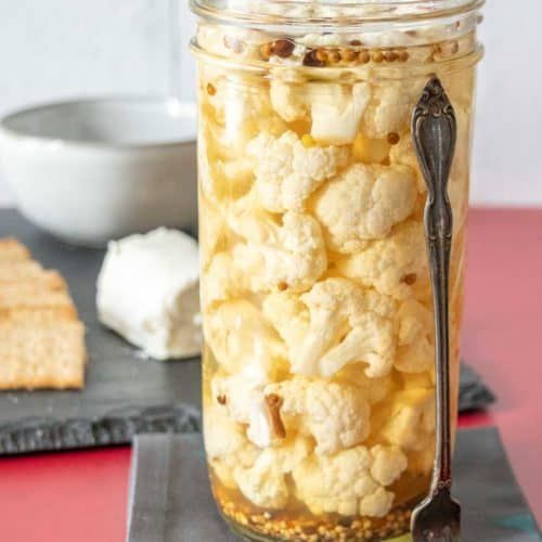 a glass jar filled with cauliflower next to crackers