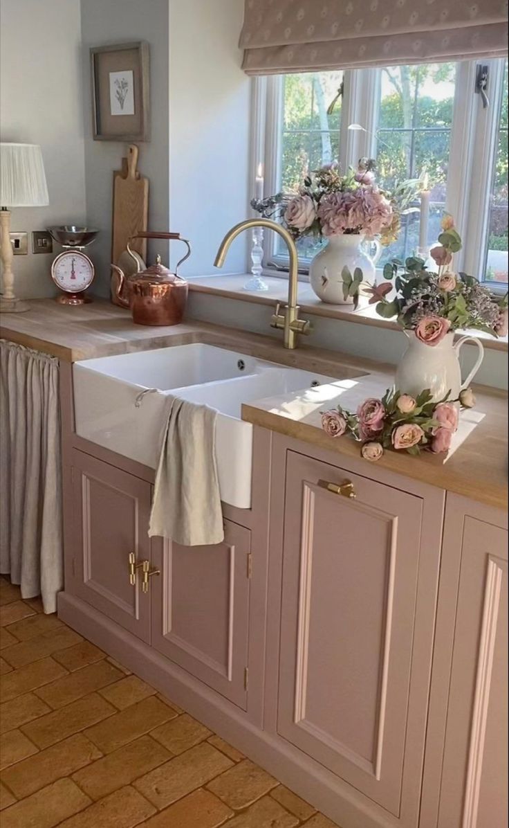 a kitchen with pink cabinets and flowers on the window sill in front of the sink