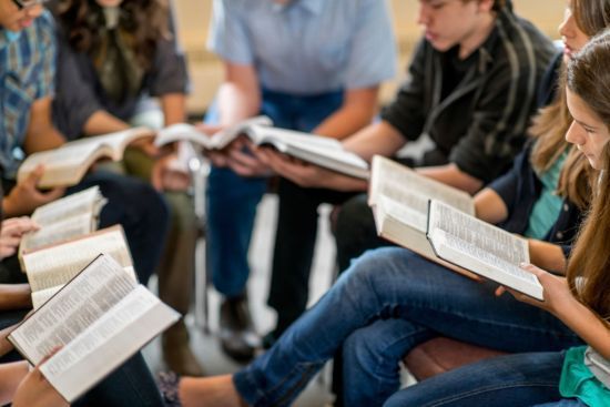 many people are sitting down and reading books with their heads turned to the side, while one person is holding an open book