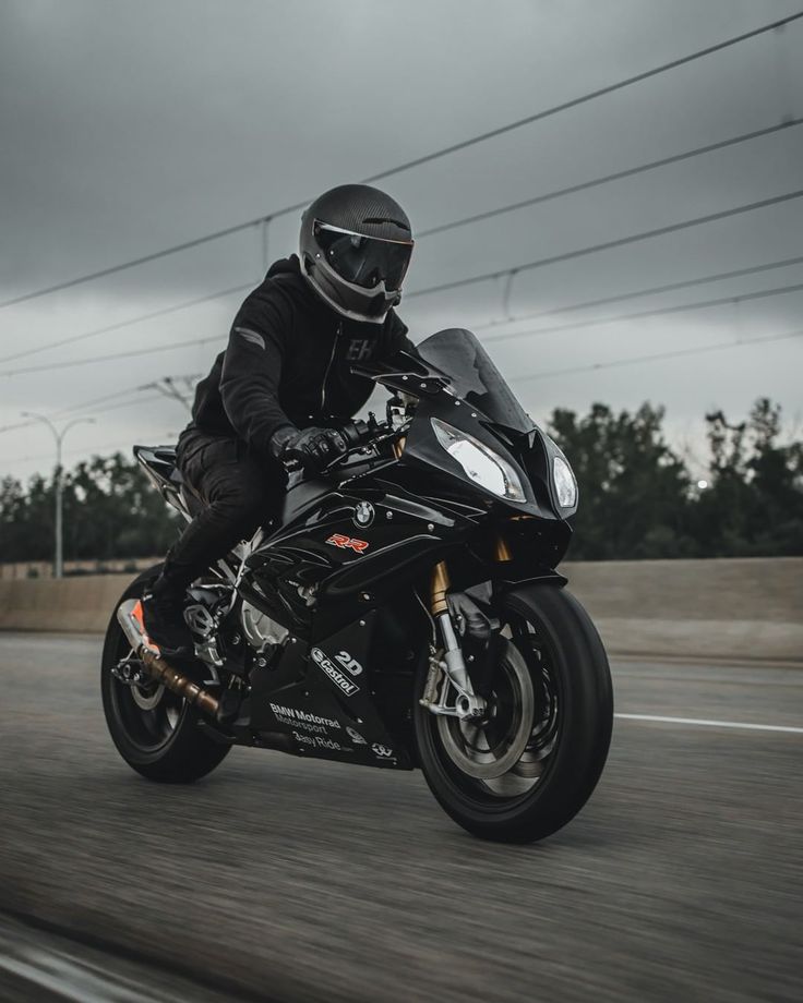 a man riding on the back of a black motorcycle down a street next to power lines