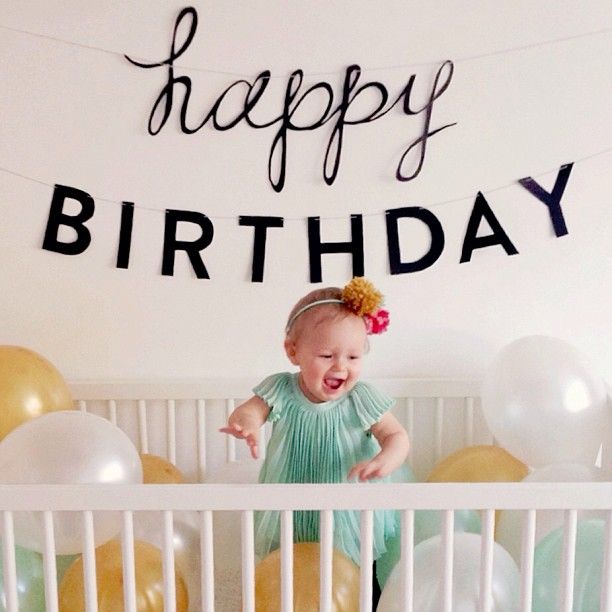 a baby in a crib with balloons and a happy birthday sign