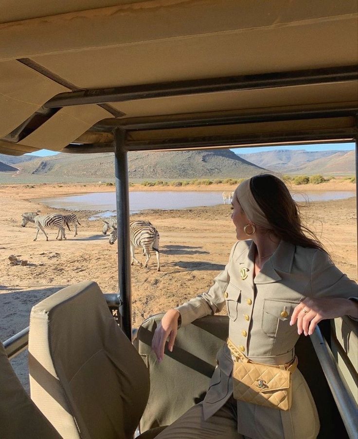 a woman sitting in the back of a safari vehicle looking at zebras and other animals