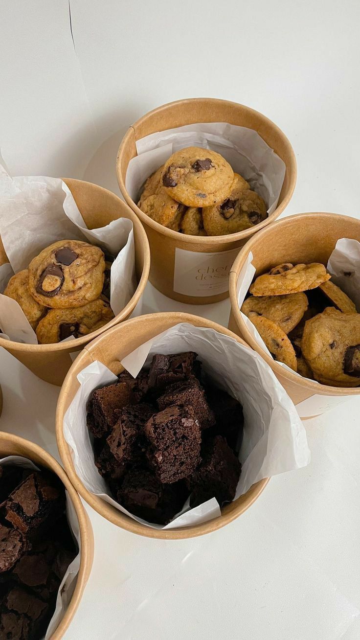 four baskets filled with different types of cookies and chocolate chip muffins on top of a white table