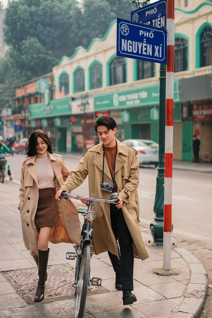 a man and woman are walking down the street with a bicycle in front of them