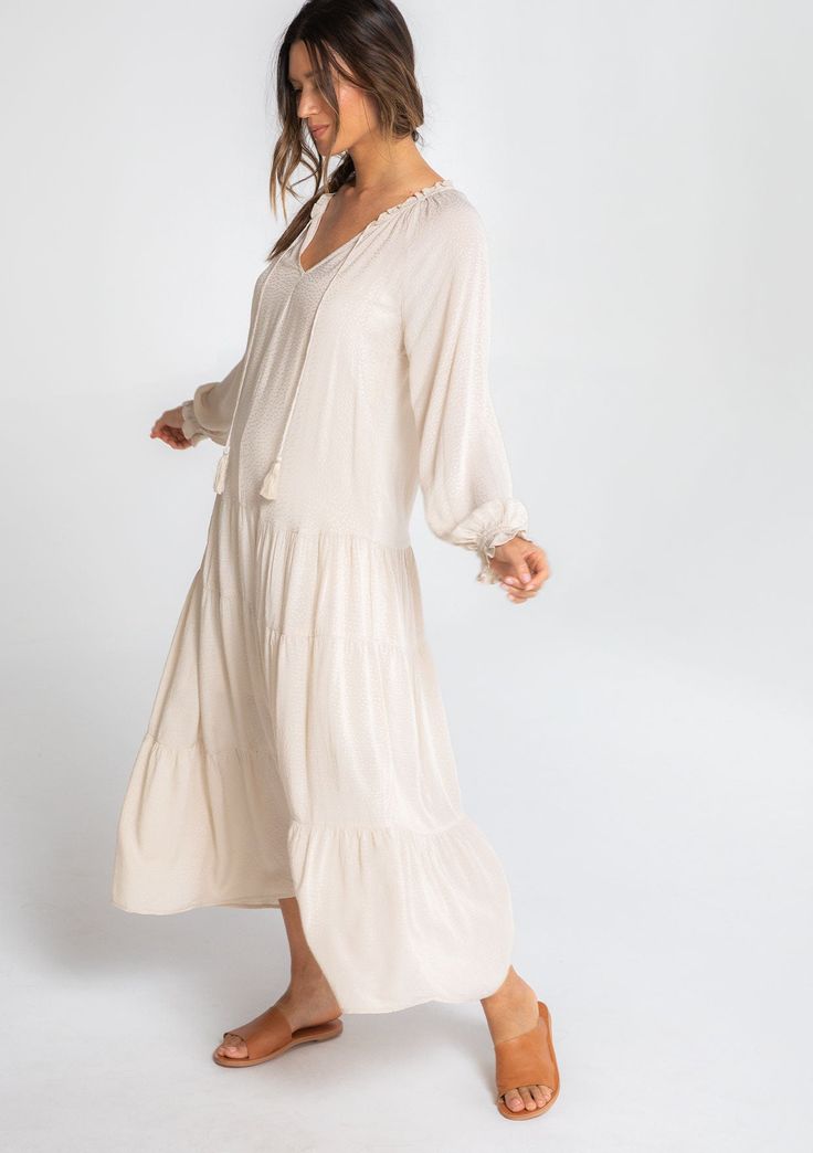 We all need that one dress that can check multiple boxes. This versatile bohemian style features a classic peasant dress silhouette, a relaxed fit, and delicate textured dot details throughout. Pair it with flat sandals for beach days, ankle boots, and a hat for date nights, or with statement heels for dinner parties. Featuring a flattering dropped waist, a flirty tiered skirt, and a pretty split v-neckline with tassel ties. Jacquard dot Relaxed fit Long raglan sleeves Ruffled wrist cuff Maxi le Flowy V-neck Peasant Boho Dress, Bohemian Tiered Dress For Vacation, Bohemian Tiered Dress For Brunch, Bohemian Midi Length Flowy Peasant Dress, Bohemian Long Sleeve Tiered Summer Dress, Bohemian Tiered Maxi Dress For Daywear, Flowing Peasant Maxi Dress For Spring, Bohemian Flowy Tiered Dress For Brunch, Bohemian Cream Tiered Maxi Dress