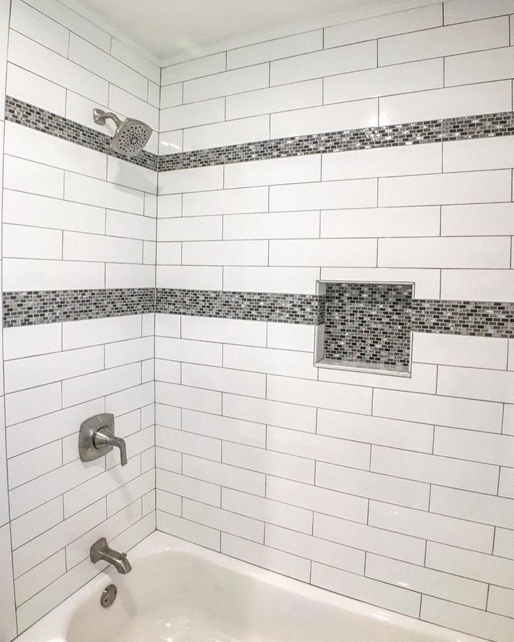 a bathtub with white tile and gray grouting on the wall next to it