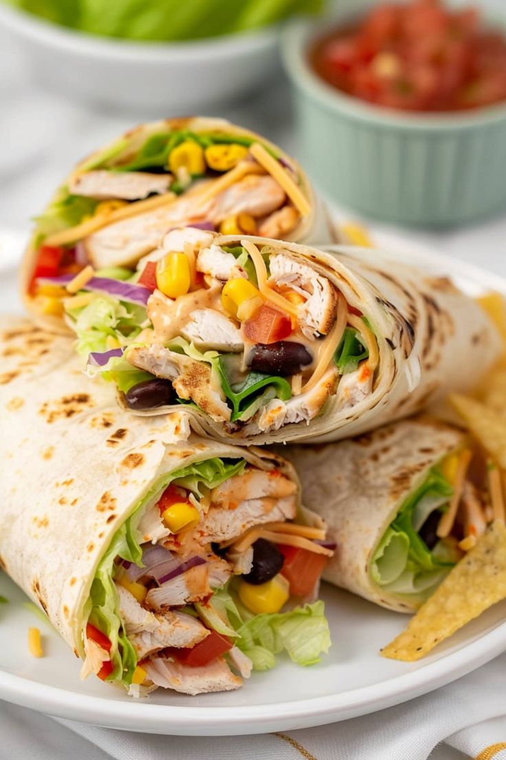 a white plate topped with two wraps filled with meat and veggies next to chips