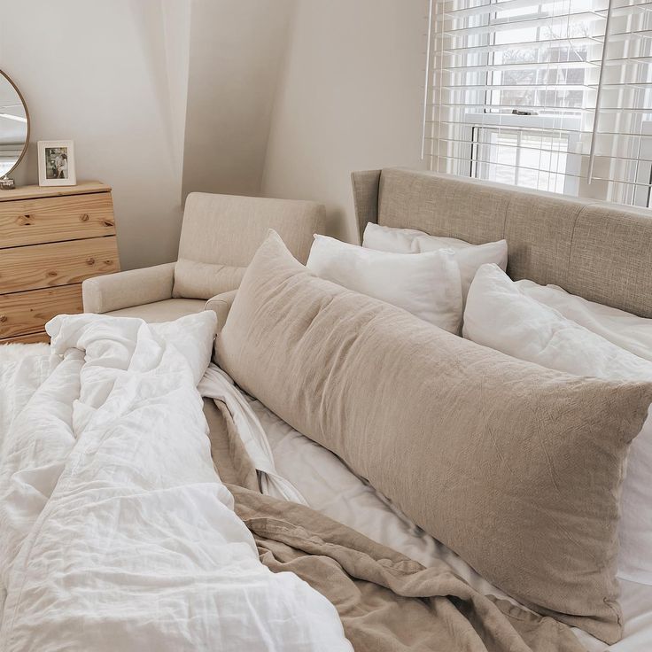 an unmade bed with white sheets and pillows in a bedroom next to a dresser