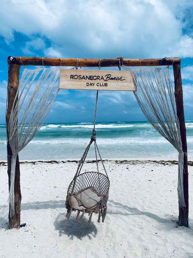 a hammock chair on the beach with a sign hanging from it's back