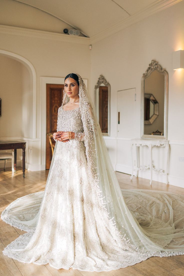 a woman in a white wedding dress standing on a wooden floor with a long veil over her head